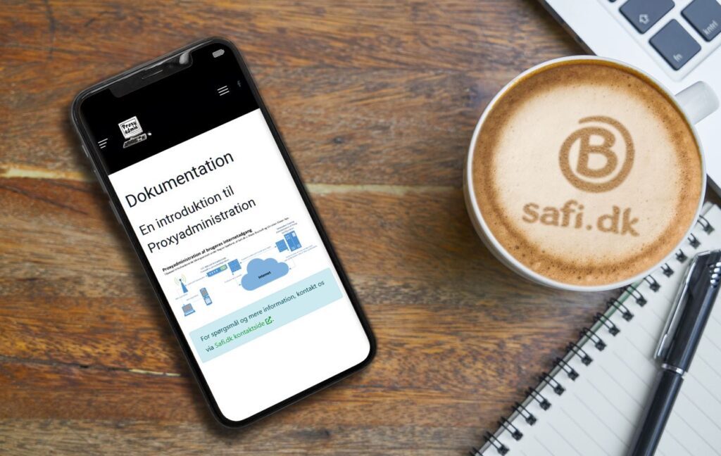 Unifi - En smartphone med en dokumentationsside for ProxyAdmin ligger på et skrivebord ved siden af en bærbar computer og en kop kaffe med "B safi.dk" trykt i skummet. Safi.dk